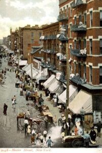 רחוב הסטר (Hester), לוואר איסט סייד (Lower East Side), מנהטן, 1900 בקרוב, גלויה מצולמת בהוצאה לא מזוהה. 
באזור הזה של ניו יורק החל מסעה הגדול של יהדות מזרח אירופה ב"עולם החדש". רצח הצאר אלכסנדר השני במרץ 1881 נתן את האות לגל של אנטישמיות, האשמות בקשירת קשר ופרעות (קיבלו את המינוח "סופות בנגב") ואשר בעקבותיהן החלה הגירה מסיבית (למעלה משני מיליון בני אדם) של יהדות מזרח אירופה לארה"ב וביסוסה של זו כמרכז היהודי הגדול בעולם של הזמן. 
ילדים בתמונה משתעשעים במים לאחר שנפרץ ברז השריפה (למטה מימיו), בד"כ זה נעשה (עבירה) כדי להפיג את חום הקיץ. כביסה מתיבשת בכל המרפסות. תאורת גז לצד "גריד" חשמל פרימיטיבי של ראשית המאה העשרים.