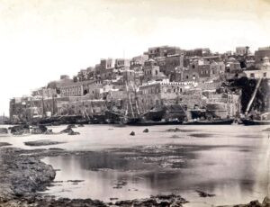 צילום מרהיב נוסף של הנמל. אף כי אינו חתום, רק מס' סידורי (148) בכתב יד בקצה השמאלי התחתון, יש יסוד להניח שגם תמונה זו היא של בונפיס. יתר על כן, ישנו סימן שמצביע על כך שאפשר שתמונה זו אף קודמת כרונולוגית לקודמתה ! בשרידי חומת העיר העתיקה שעדיין נותרו על מקומם, בימין התמונה, לשפת המים מתחת למיגדלור, ניתן להבחין במבנה מעוגל (מיצדית ?) שבתמונה הקודמת כאמור, כבר לא קיים. ואם אכן כך, אפשר להניח במידה רבה של ודאות שתמונה זו צולמה בשלהי שנות השישים (של המאה ה 19) !