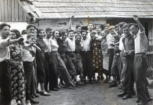 14 ביוני 1936.
תמונה מרשימה של פרץ שמחה בקרב הצעירים החלוצים הללו. כדאי לשים לב לשתי צעירות, זו במרכז שרגלה מונפת (שמעון לשמאלה) וזו השלישית משמאל, שתיהן לובשות מכנסיים, מראה יוצא דופן ובעל אמירה לבנות התקופה.