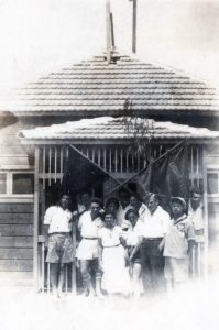 בפתח צריף חדר האוכל בחדרה, החברים מוצאים את הזמן עתה לפעילות אידיאולוגית החביבה כ"כ בשוה"צ - הנפת דגלים עם מסרים מתאימים המתוכננת לחגיגות האחד במאי (1934) במושבה (חדרה).