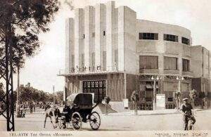 בית האופרה "מוגרבי" (לימים קולנוע "מוגרבי") במפגש הרחובות פינסקר (מימין), בן יהודה (משמאל) ואלנבי (מאחור), גלויה בהוצאת "האחים אליהו". המבנה הייחודי בסגנון ה"אר דקו", בתכנונו של האדריכל יוסף ברלין, נחנך בפברואר 1930 והיה עד מהרה למרכזי בחיי הקהילה של תל אביב. 
האולם הקטן שלו בקומת המרתף היה לבית הקבע להופעותיו של ה"אהל" (גם של "הבימה" ועוד) בתל אביב ושימש אותו עד להקמת בית ה"אהל" ברחוב בילינסון ב 1940. בימין התמונה (מתחת למנורות) ניתן להבחין בכרזת פרסום להצגת התיאטרון "שאפ" ! (הצגת הבכורה שלה התקיימה כאמור בחודש יולי 1932).