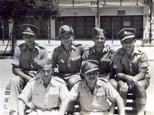 קיץ 1944, החברים בחזית קפה-בר "הוברמן" ברמת גן, כולם מגויסים. מרדכי עופר, למעלה שני משמאל, במדי נוטר, השאר במדי יחידות שונות של "הבריגדה היהודית" בצבא הבריטי שזה אך קמה: בני אטלס למעלה שני מימין, דב איטמן למטה מימין ואברהם אלסטר לידו. קפה "הוברמן" שכן במורד רחוב הרצל, בפינת רחוב דוד (על מקומו קם בנין  קופ"ח "מכבי"), והיה מרכז בילוי בורגני נודע בזמנו. 
בדומה לשאיפות ההתגיסות של היישוב כגוף אחד המזוהה לאומית במלחמת העולם הראשונה (ל"גדודים העבריים"), אז זיהו הבריטים את הפוטנציאל הגלום בגוף כזה למימוש השאיפות הלאומיות ודחו את הקמתו ככל האפשר (ומיהרו לפרקו מיד עם סיום המלחמה), גם במקרה זה הם פעלו בצורה דומה ודחו את הקמת "הבריגדה" עד למעשה לשלב בו הכרעת גרמניה כבר נראתה בלתי-נמנעת. אלה רגעים אחרונים של זהות אינטרסים בין היישוב והשלטון הבריטי אל מול האויב המשותף ועם תום המלחמה יחל השלב הקריטי של המאבק על השליטה בא"י.