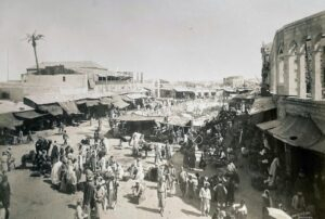 מבט מהכיוון ההפוך (מדרום-מזרח) על שוק העיר התוסס (הוא ה"באזר" האוריינטלי, ולימים "כיכר השעון") בתצלום מרשים  של צלמי "אמריקן קולוני" (American Colony) משלהי המאה ה 19. במרכז מאחור, בולט על רקע סביבתו, המבנה הדו-קומתי של מלון-הדרכים המופיע גם בתצלומו של בונפיס. כאשר הוקם בשלהי שנות השישים של המאה ה 19 כאמור, היה ממבשריה של הבניה מחוץ לחומות (כיום הוא מאכלס את "מרכז הגלישה העירוני", בפינת הרחובות נחום גולדמן וזלדה שניאורסון). במרכז הרחבה, בצד שמאל, נראית קשת הכניסה המפוארת למסגד "מחמודיה" (שני עמודים בודדים מאחוריה), היא כניסת ה"מכובדים" שיוחדה לבאי ה"סאריה". מעל לקשת נראה גג הרעפים המאורך של ה"קישלה" - הקסרקטין הצבאי ובית המעצר העות'מנים (משטרת המרחב לאחר קום המדינה ובמשך עשרות שנים וכיום מלון "סטאי").
