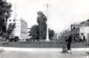1940 בקרוב, כיכר סלמה בצומת שדרות קינג ג'ורג' (שד' ירושלים כיום) ודרך סלמה (הדרך ההסטורית שהובילה מיפו לכפר סלמה ומשם ללוד), מבט לאורך השדרה מדרום לצפון (הכניסה לדרך סלמה ליד הכרכרה בימין התמונה). הכיכר הוקמה באמצע שנות העשרים של המאה ה 20 עפ"י מיטב המסורת הבריטית של כיכרות מעגליות לוויסות התנועה בצמתים מרכזיים. הכיכר נהרסה ב 1970 (בקרוב) כחלק מתהליך מקיף של החלפת השיטה ה"מיושנת" ברימזור "מודרני". 
בנין הדואר המרכזי של יפו (שד' ירושלים 12) בולט בשמאל התמונה. המבנה, בתכנון האדריכל הבריטי אוסטן סנט בארב האריסון, נחנך בשנת 1931 ומשמש בתפקידו המקורי עד היום (2025). צילום של "פלפוט" כהכנה להפקת גלויה.